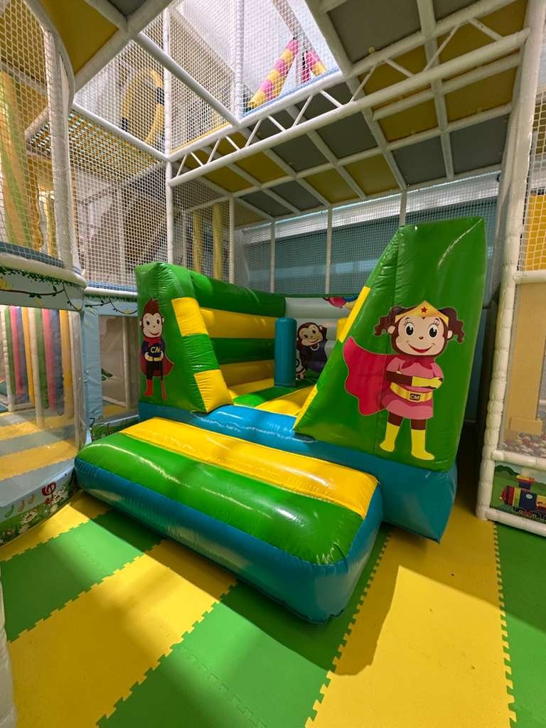 Green-and-yellow inflatable slide beneath a netted multilevel play structure at Cheeky Monkeys.